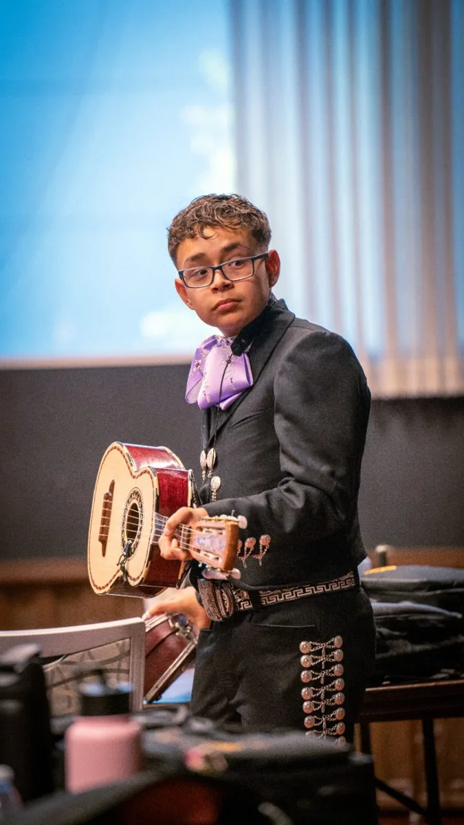A young musician in a mariachi suit holding a guitarrón.