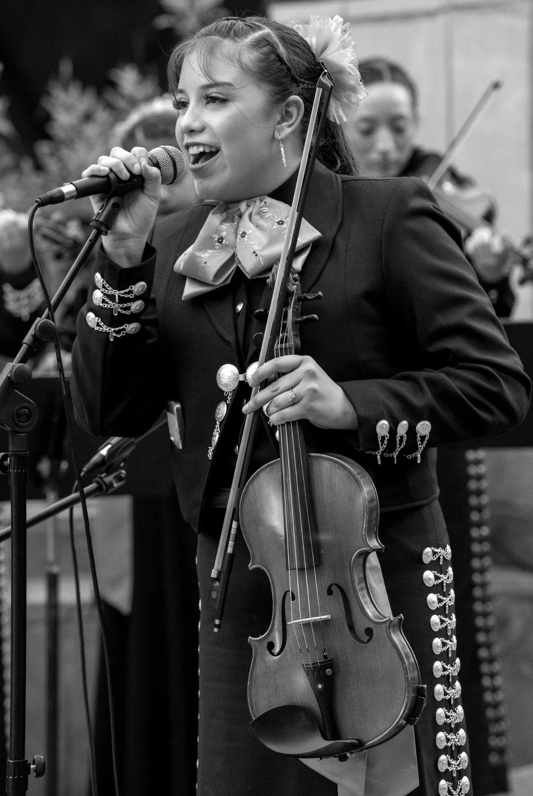 Black-and-white concert image of a Harmony Project student singer with orchestra musicians in the background