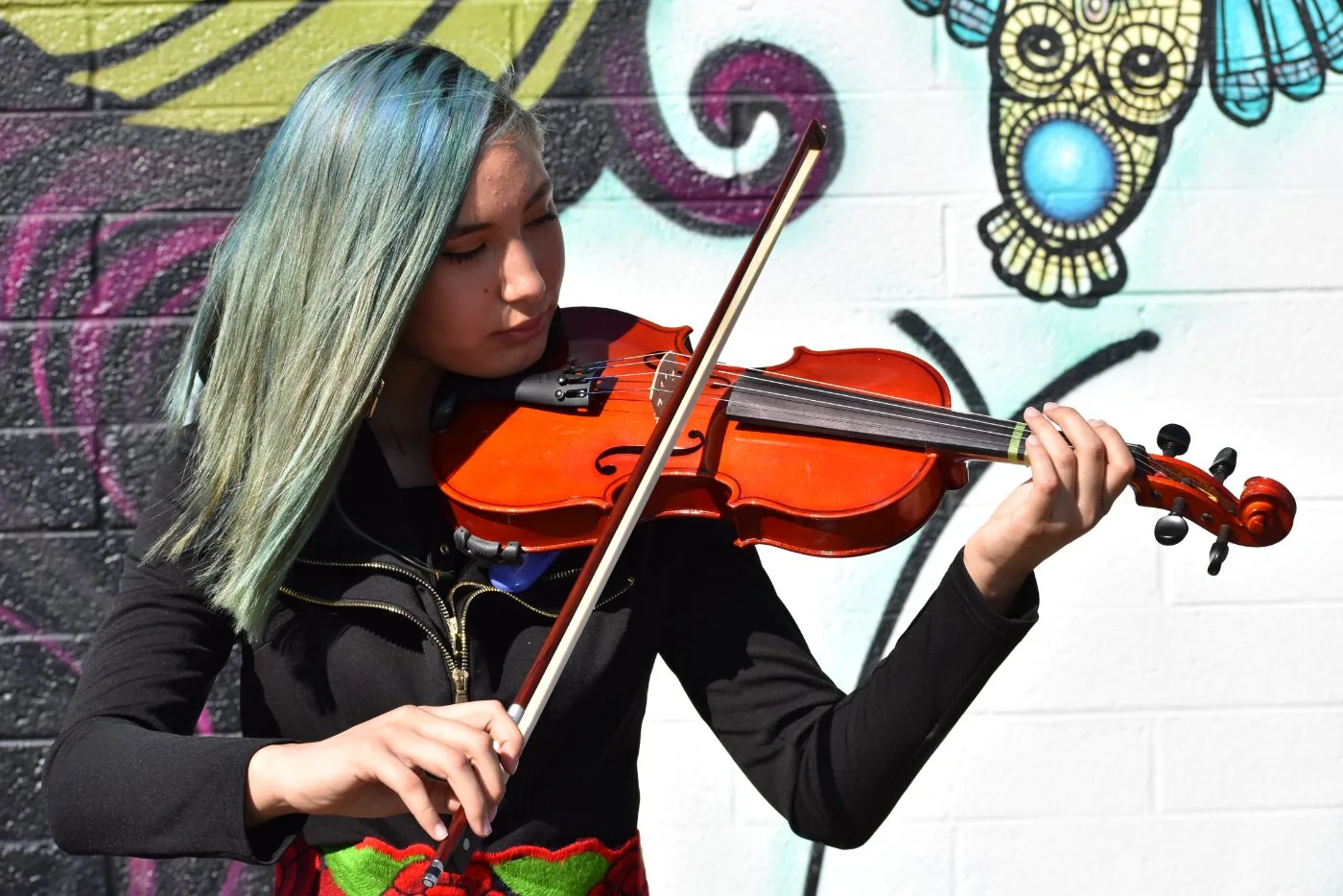 A student playing violin in front of a Phoenix mural